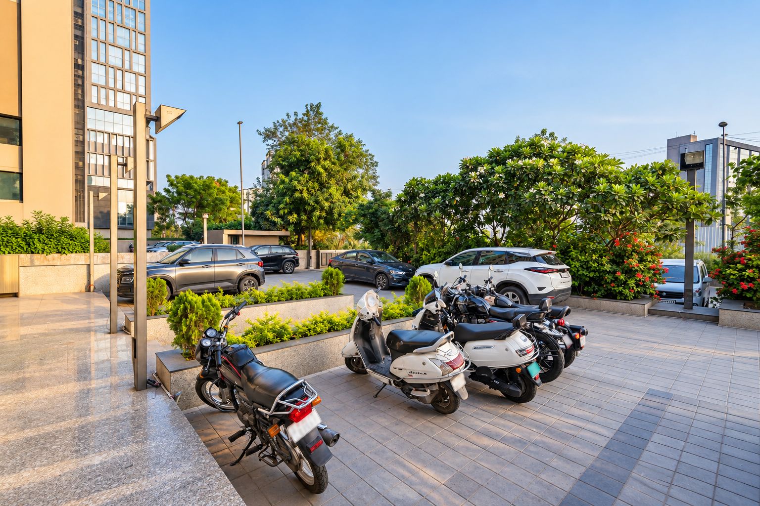 A parking area with multiple motorcycles and cars, surrounded by greenery and modern buildings.