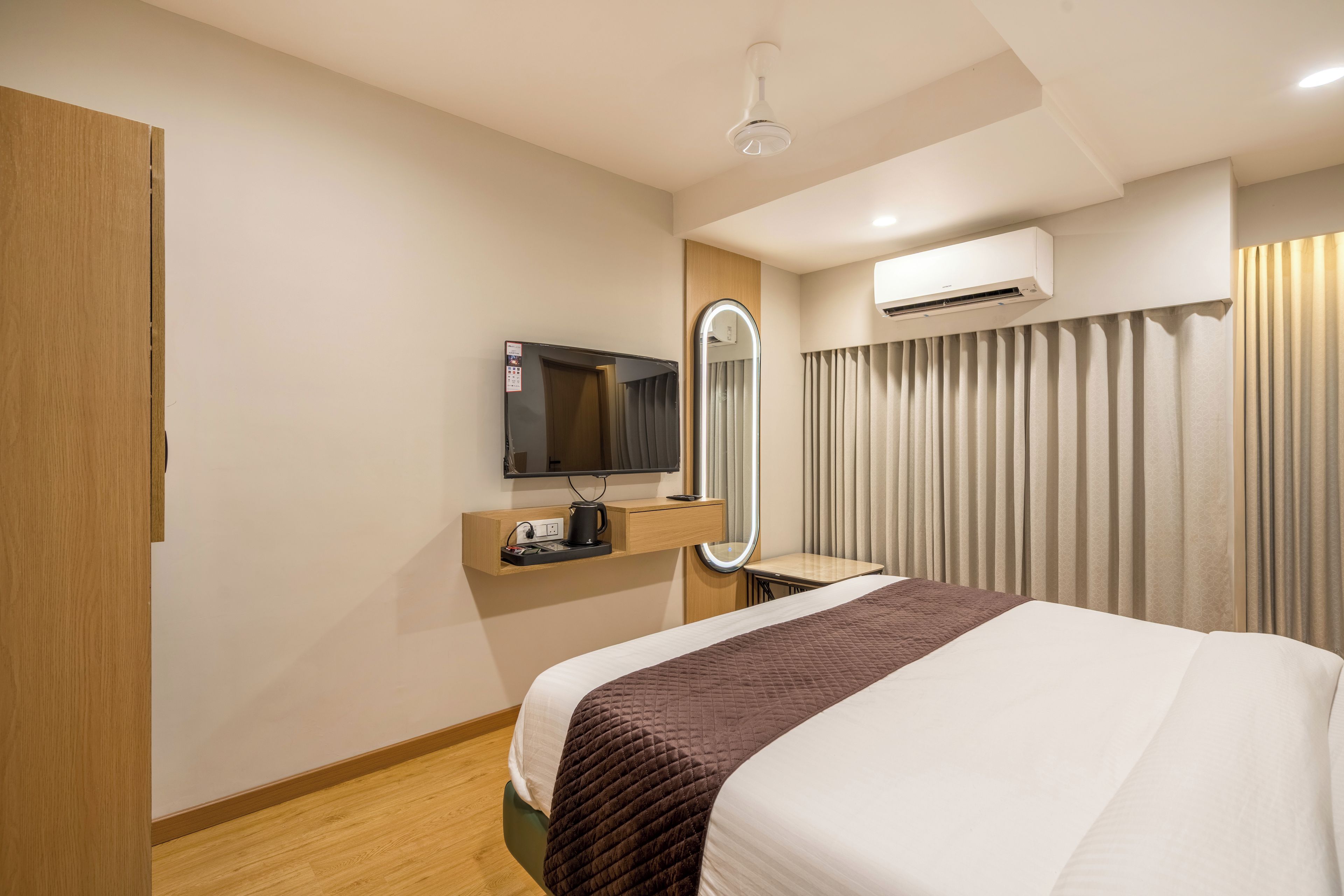 Habitación de hotel con cama, televisión, espejo, aire acondicionado y ventana con cortinas.