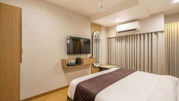 Habitación de hotel con cama, televisión, espejo, aire acondicionado y ventana con cortinas.