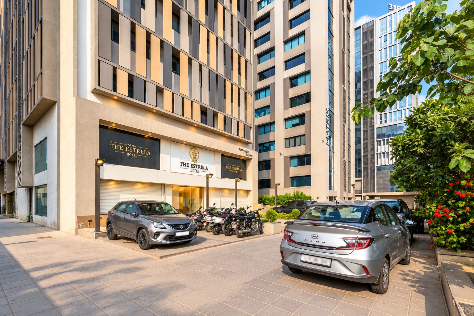Een hotel met een moderne gevel, geparkeerde auto's en een heldere lucht.