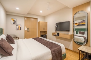 A hotel room with a bed, a desk, a mirror, a TV, and artwork on the walls. - The Estrela Hotel (Ahmedabad)