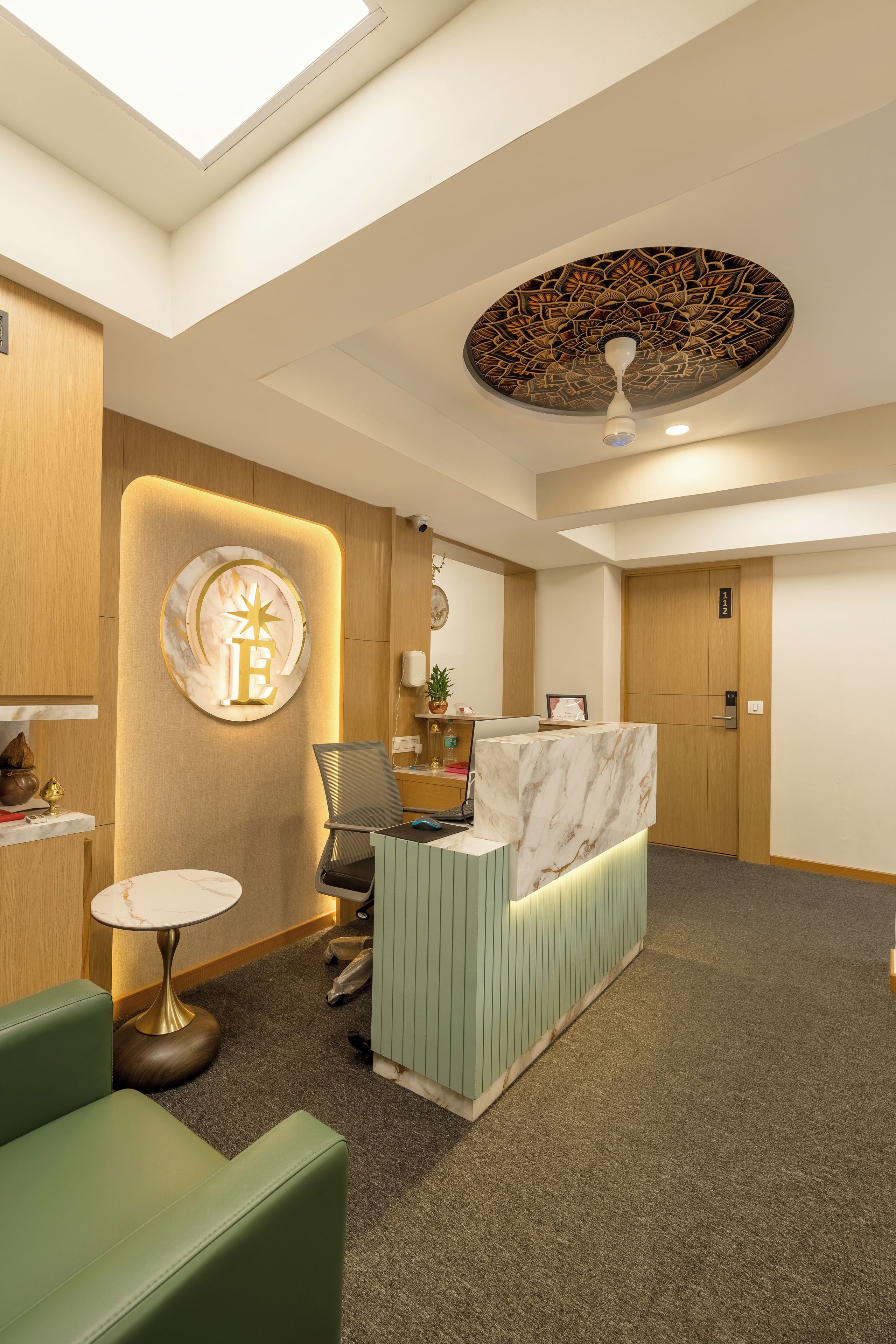 A reception area with a marble counter, a green sofa, a small round table, and a ceiling with a decorative pattern.