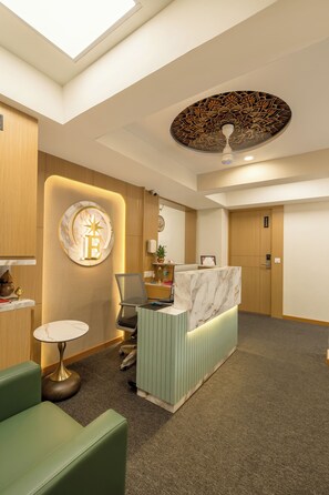 A reception area with a marble counter, a green sofa, a small round table, and a ceiling with a decorative pattern.