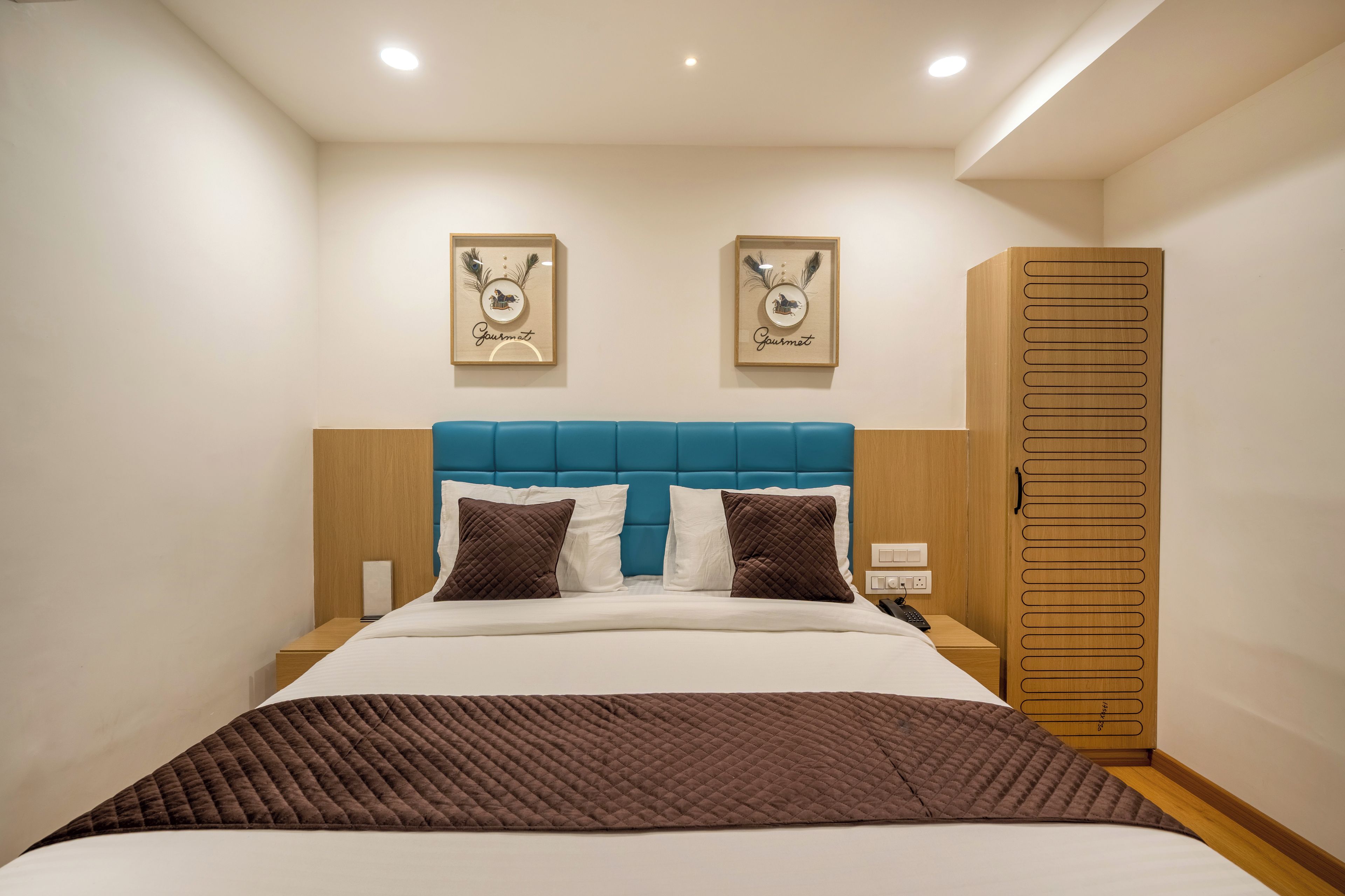 A hotel room with a bed, a nightstand, a wardrobe, and two wall-mounted artwork pieces.