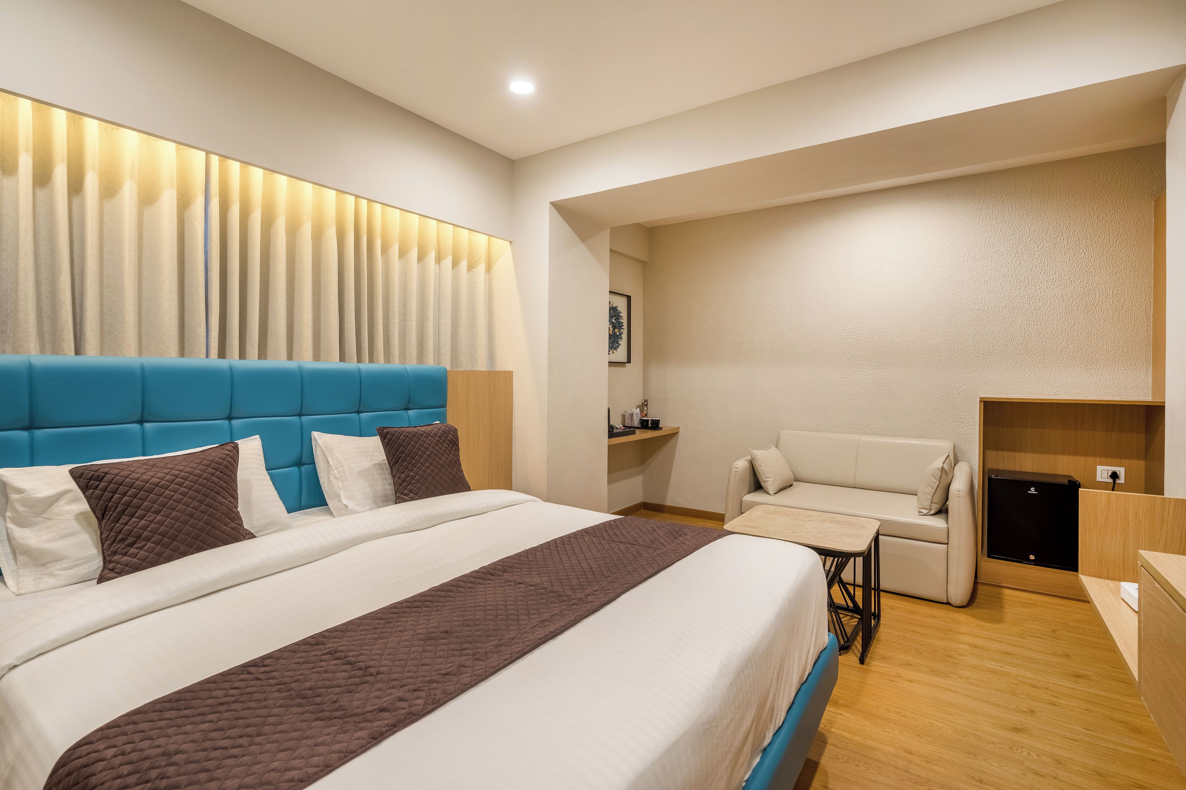 Una habitación de hotel moderna con una cama grande, un cabecero azul, un área de descanso y una mesita.