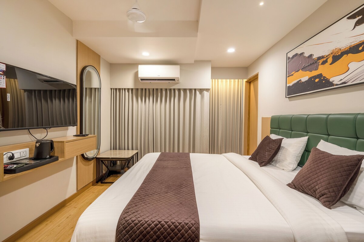 Una habitación de hotel con cama, escritorio con hervidor, televisión y aire acondicionado.