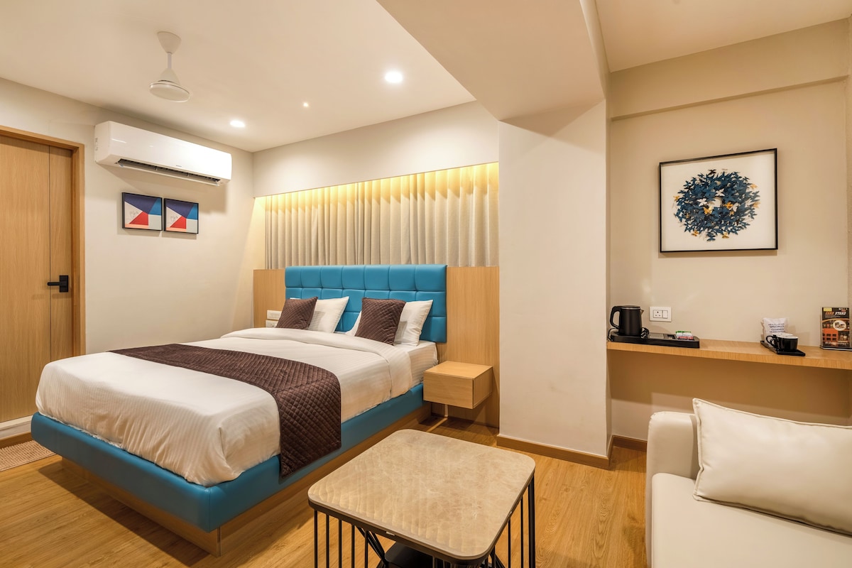Una habitación de hotel moderna con una cama grande, mesita de noche y una pequeña zona de estar.