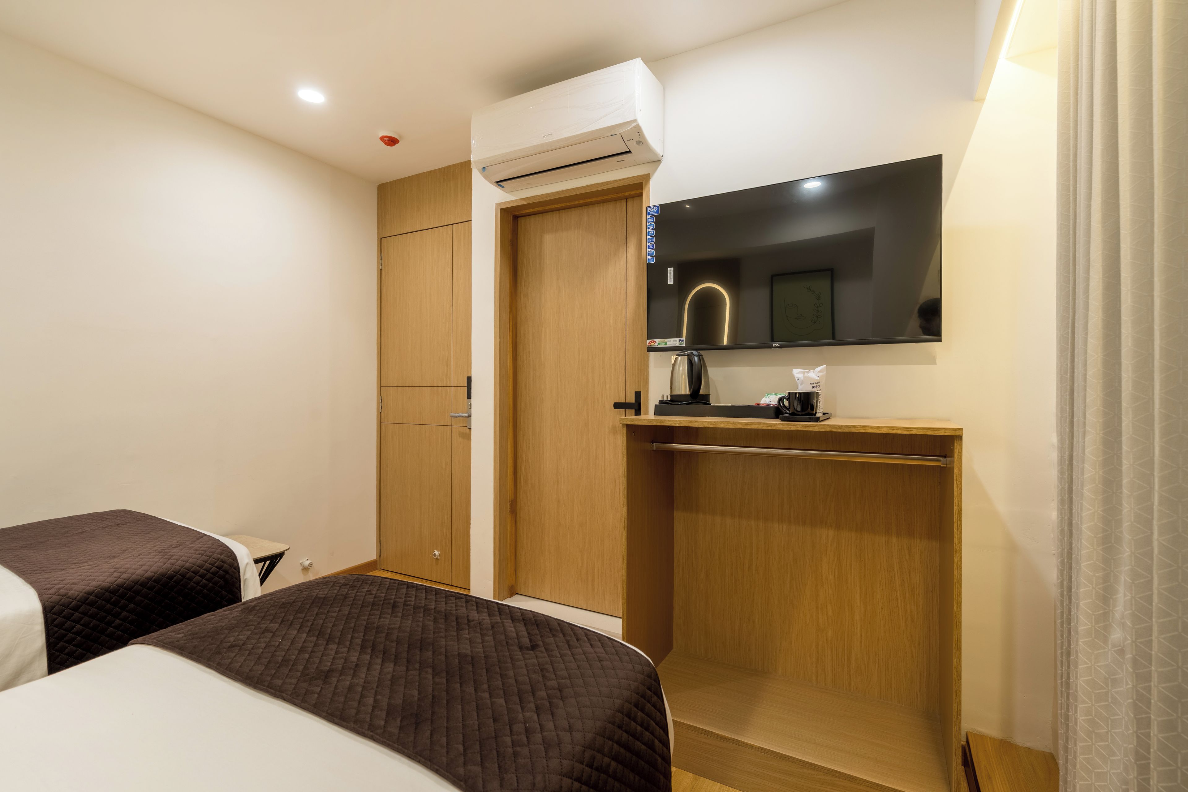 Een hotelkamer met een bed, een bureau met een waterkoker, een spiegel en een airconditioning.