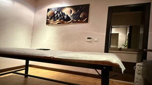 A room with a wooden floor, a bed with a white sheet, a painting on the wall, a mirror, and a white appliance. - Suites by Sunday Avenue in the Heart of Riyadh (Riyadh)