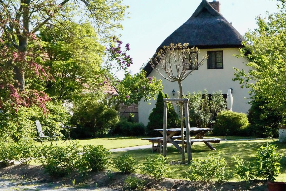 A traditional house with a thatched roof, surrounded by a well-maintained garden with a picnic table and a wooden swing set.