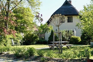 A traditional house with a thatched roof, surrounded by a well-maintained garden with a picnic table and a wooden swing set. - Fischerhus Krummin - Thatched-roof house with a private sauna (Krummin)