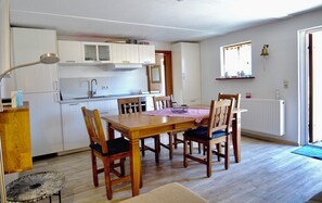 A compact kitchen with white cabinets, a wooden dining table with chairs, and a small round table with a lamp. - Fischerhus Krummin - Thatched-roof house with a private sauna (Krummin)