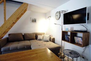 A living room with a sofa, a wooden table, a floor lamp, a television, and a bookshelf. - Fischerhus Krummin - Thatched-roof house with a private sauna (Krummin)