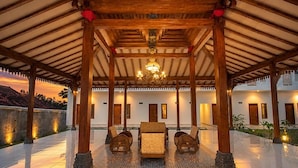 Uma área externa coberta com um pavilhão de madeira, uma mesa central com cadeiras e um candelabro.