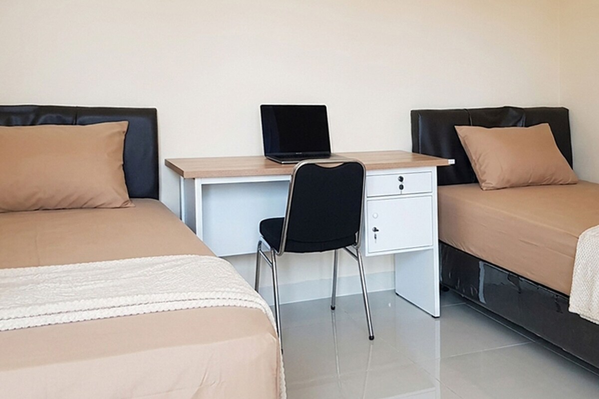 A room with two beds, a desk with a laptop, and a chair.