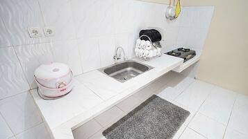 A kitchen with a white countertop, a sink, a dish rack, and a kettle.