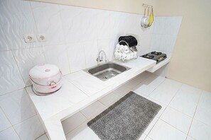 A kitchen with a white countertop, a sink, a dish rack, and a kettle.