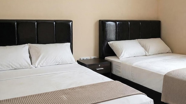 Quarto de hotel com duas camas, cada uma com cabeceira preta e roupa de cama branca. Há uma pequena mesa de cabeceira com gaveta e uma luminária.