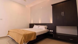 A bedroom with a bed, a wardrobe, and a television. - Ajantha Komforts By Avenya (Bengaluru)