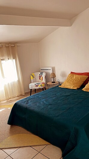 Ein Schlafzimmer mit einem Bett, einem Sessel, einem Tisch und einem Fenster mit Vorhängen.