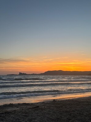 Ein Strand bei Sonnenuntergang mit Wellen, einem entfernten Landteil und einem klaren Himmel.
