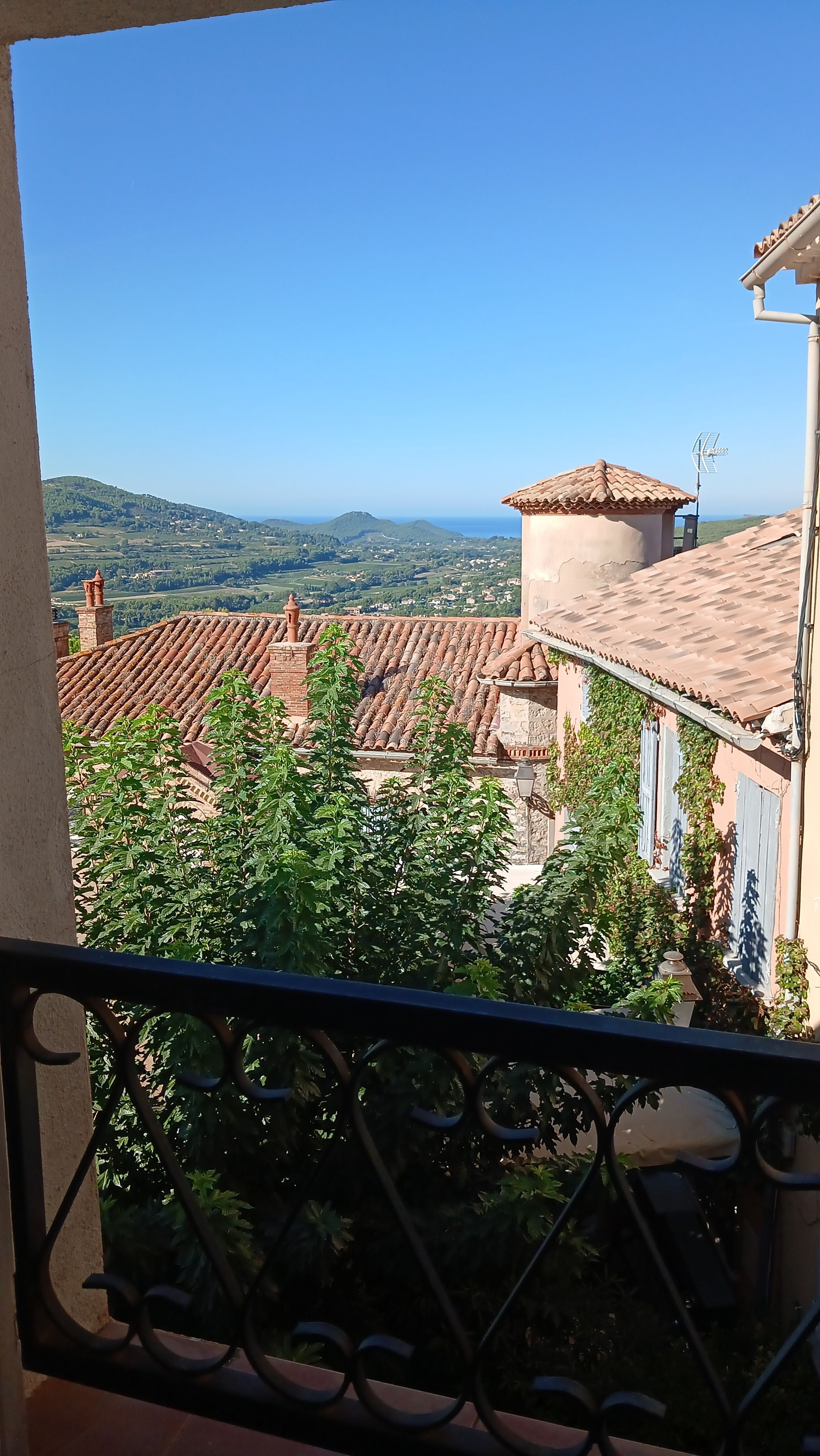 A balcony with a view of terracotta-roofed buildings and a distant landscape.