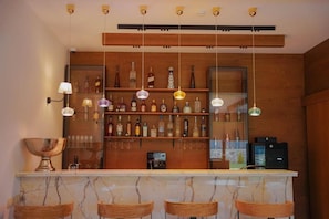 Una zona de bar con encimera de mármol, sillas de madera, lámparas colgantes y estanterías llenas de botellas.
