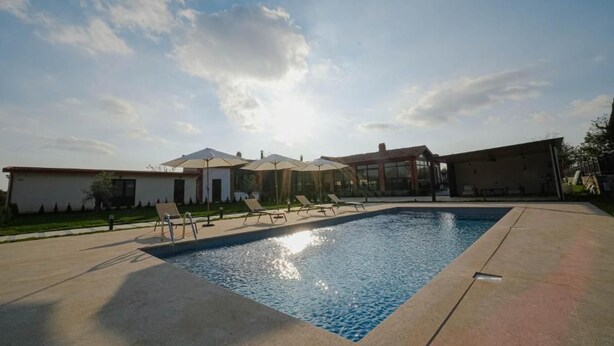 A swimming pool with lounge chairs and umbrellas, surrounded by buildings with a clear sky above. - Mikheilis Marani Boutique Hotel  (Kvareli)