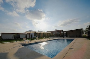 Una piscina con sillas de descanso y sombrillas, rodeada de edificios bajo un cielo despejado.