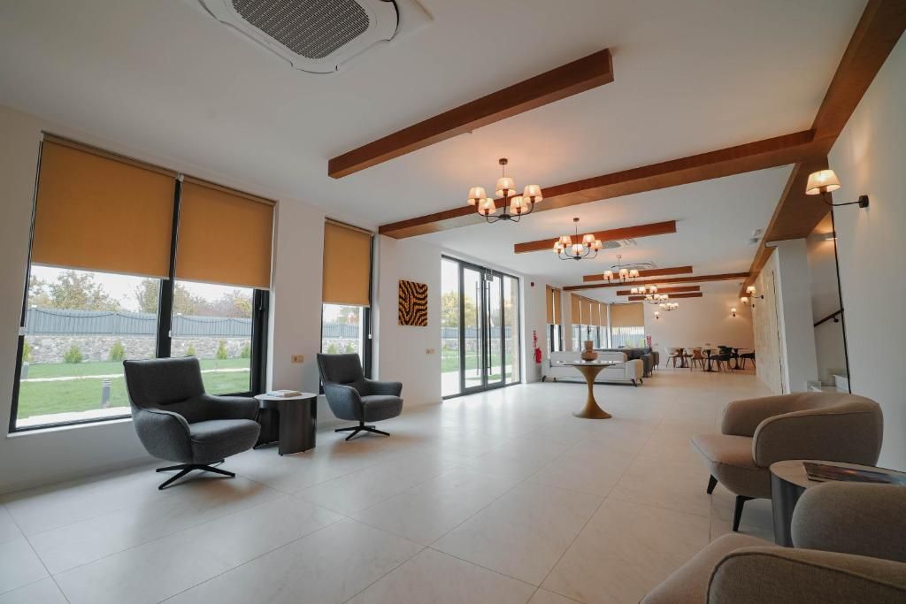 A spacious room with large windows, a modern chandelier, and a dining area in the background.