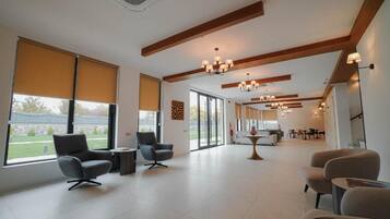 A spacious room with large windows, a modern chandelier, and a dining area in the background.