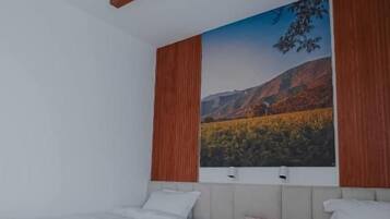 Une chambre avec deux lits, une tête de lit en bois, un tableau représentant un paysage et une petite table.