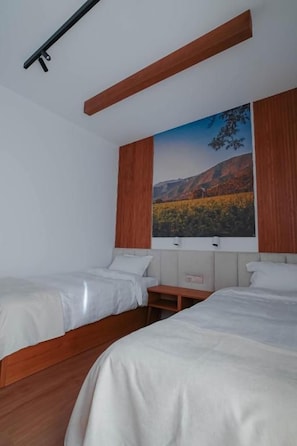 Une chambre avec deux lits, une tête de lit en bois, un tableau représentant un paysage et une petite table.