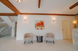 A spacious room with a staircase, two armchairs, a round table, and a painting on the wall.
