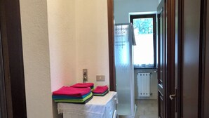 A laundry area with a washing machine, a radiator, and a window with a view of trees. - Vrbo Property (Magognino)