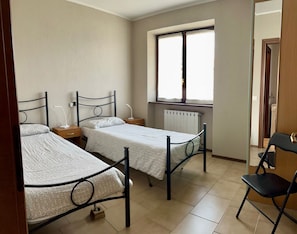 A room with two beds, a window, a radiator, and a chair.