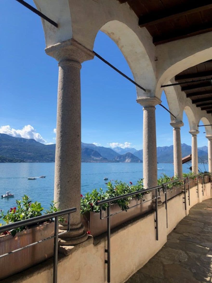 A covered outdoor area with stone columns and a view of a lake with boats.