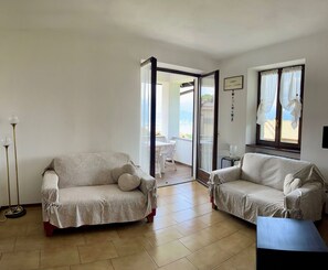 A living room with two sofas, a floor lamp, and a view through a glass door to an outdoor area.