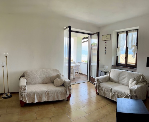 A living room with two sofas, a floor lamp, and a view through a glass door to an outdoor area.