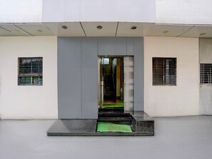 A modern building entrance with a glass door, a small set of steps, and a green mat. - Deluxe Hotel Sai Dhanlaxmi (Rahata)