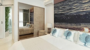 A bedroom with a bed, a nightstand, a lamp, a large window, and a view of the ocean. - AQUA Boutique Hotel- Ocean View Suites (Glacis)