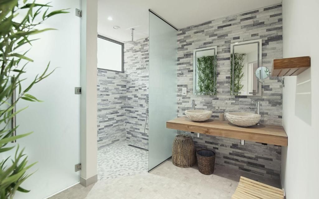 Un baño de diseño moderno, con una pared de mosaicos de piedra, un tocador de madera con lavabo integrado y un espejo con plantas.