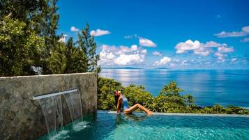Una persona descansando junto a una piscina con cascada y vista al océano.