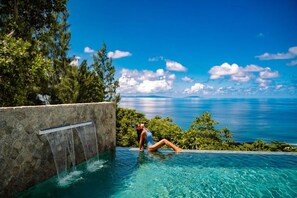 Una persona relaxant-se a la piscina amb una cascada i vista a l'oceà.