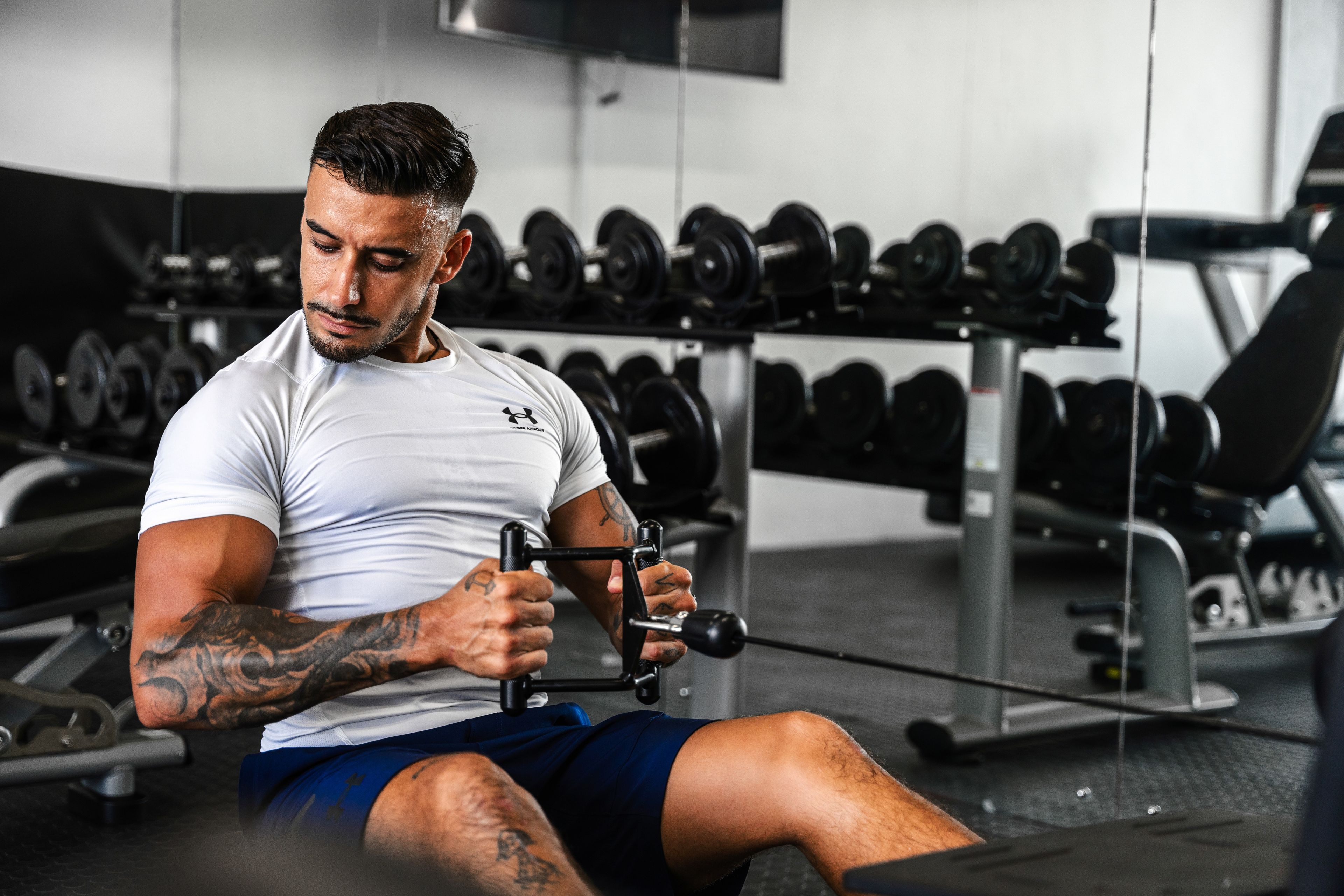 Un hombre haciendo ejercicio con una máquina en un gimnasio, con varios pesas al fondo.