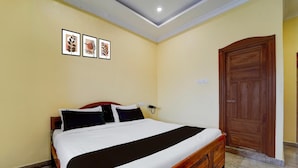 A hotel room with a single bed, a wooden wardrobe, a wall-mounted telephone, and three framed pictures. - Hotel O Karaikal Beachview (Karaikal)