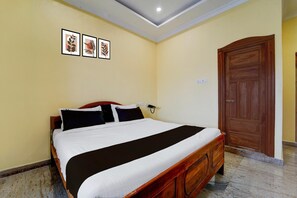 Una habitación de hotel con una cama individual, un armario de madera, un teléfono de pared y tres cuadros enmarcados.