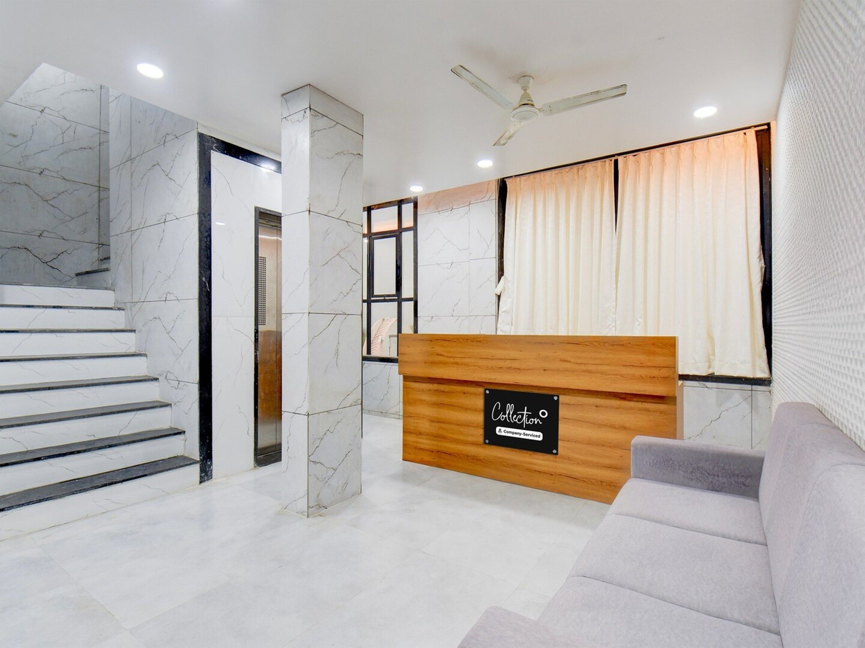 A reception area with a marble staircase, a wooden reception desk, and a grey sofa.