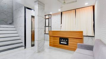 A reception area with a marble staircase, a wooden reception desk, and a grey sofa.