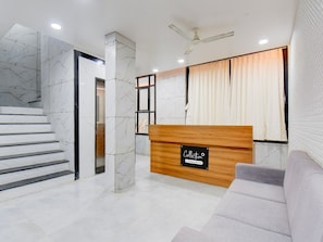 A reception area with a marble staircase, a wooden reception desk, and a grey sofa. - Collection O Aurangabad Shendra Midc (Chhatrapati Sambhajinagar)